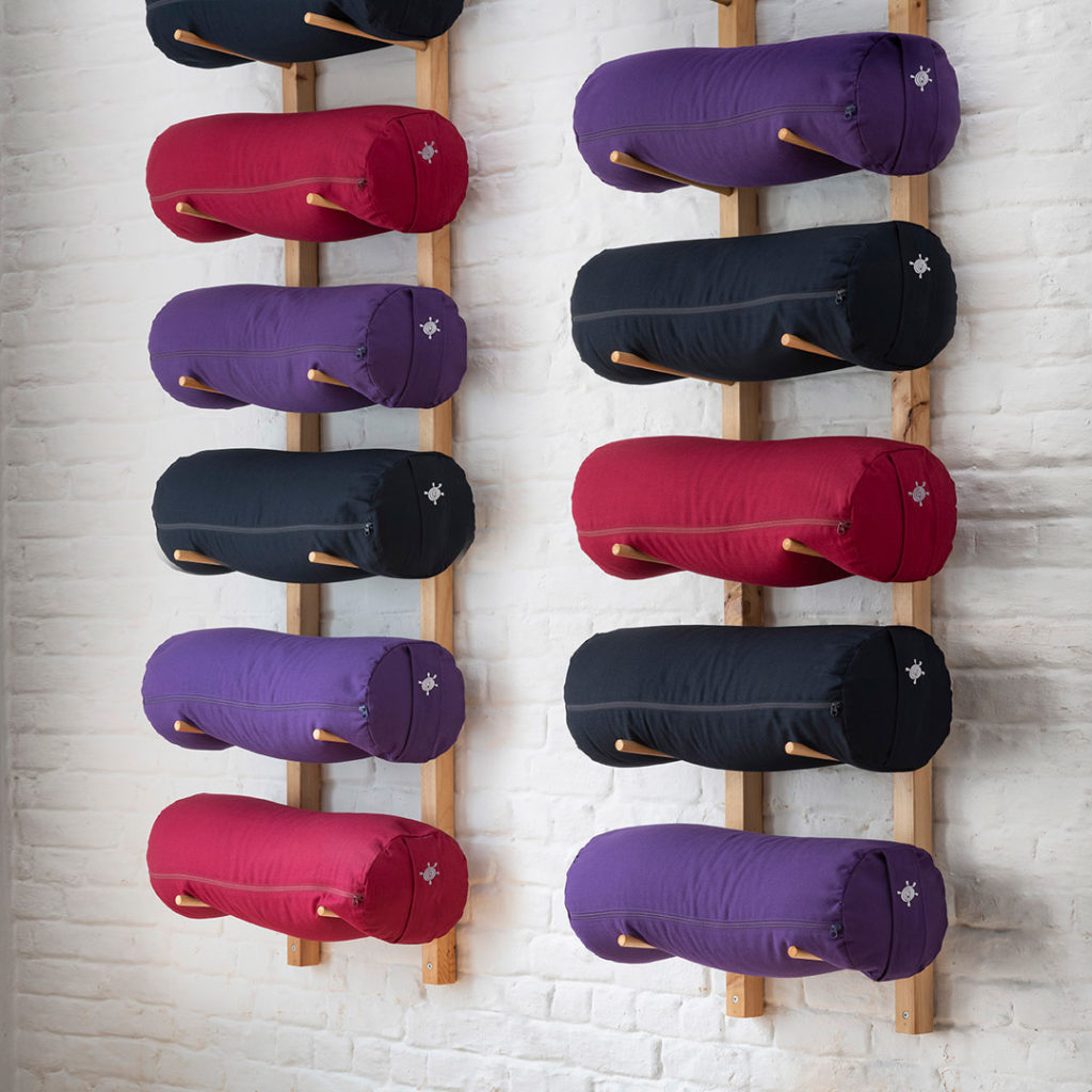 Kurma yoga bolsters stored on wooden rack